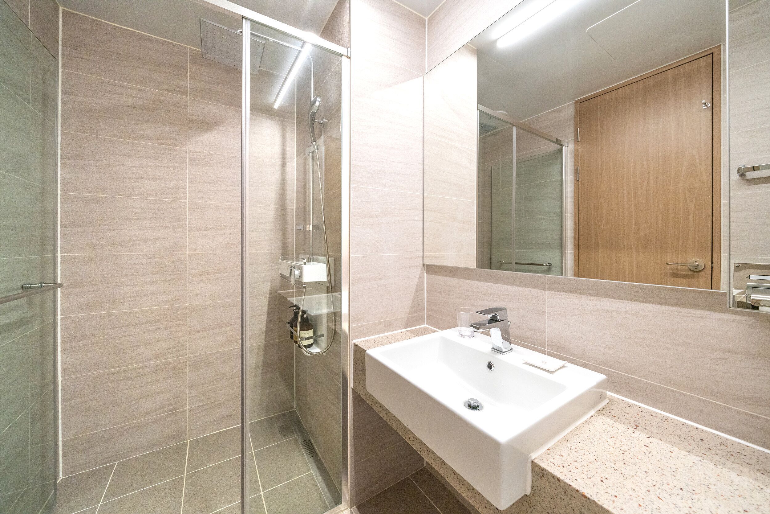 Un baño moderno con ducha envuelta en vidrio, un lavabo blanco y un espejo grande.