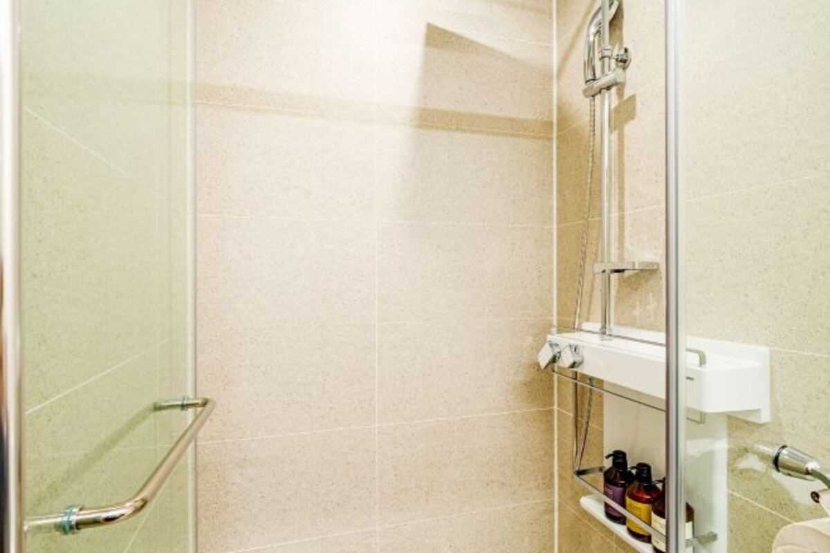 Une douche avec une porte en verre, une barre d’appui et une étagère pour les articles de toilette.