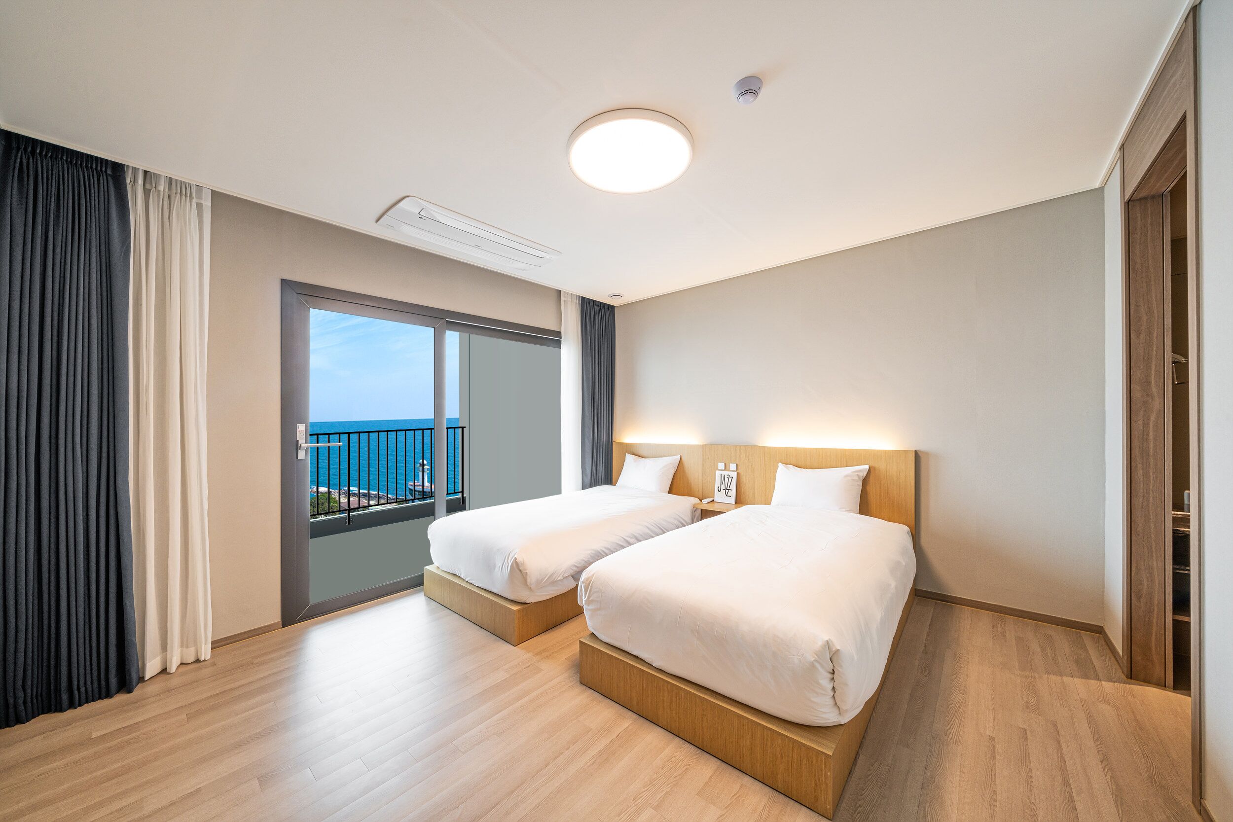 Una habitación de hotel con dos camas, un balcón con vistas y un ventanal grande.