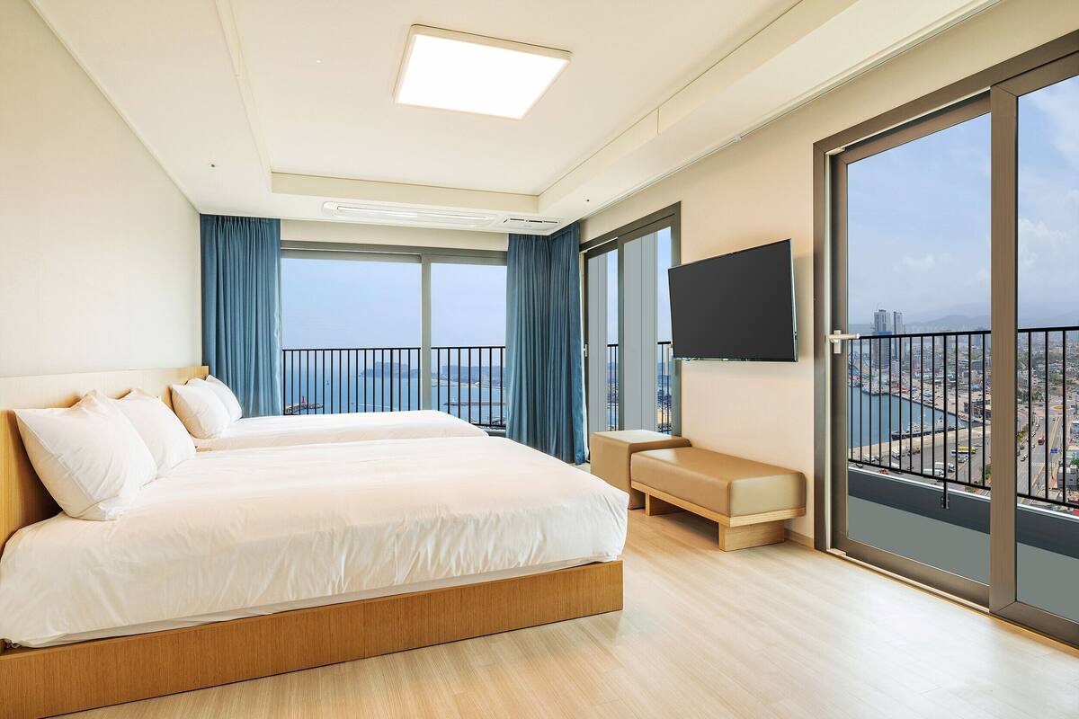 Habitación de hotel moderna con una cama grande, un pequeño rincón de descanso, televisión y balcón con vistas a la ciudad.