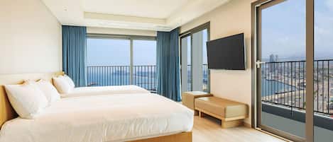 Habitación de hotel moderna con una cama grande, un pequeño rincón de descanso, televisión y balcón con vistas a la ciudad.