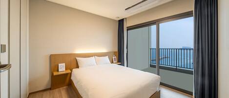 Habitación de hotel con una cama grande, una mesita de noche, aire acondicionado en la pared y vistas al mar desde un balcón.