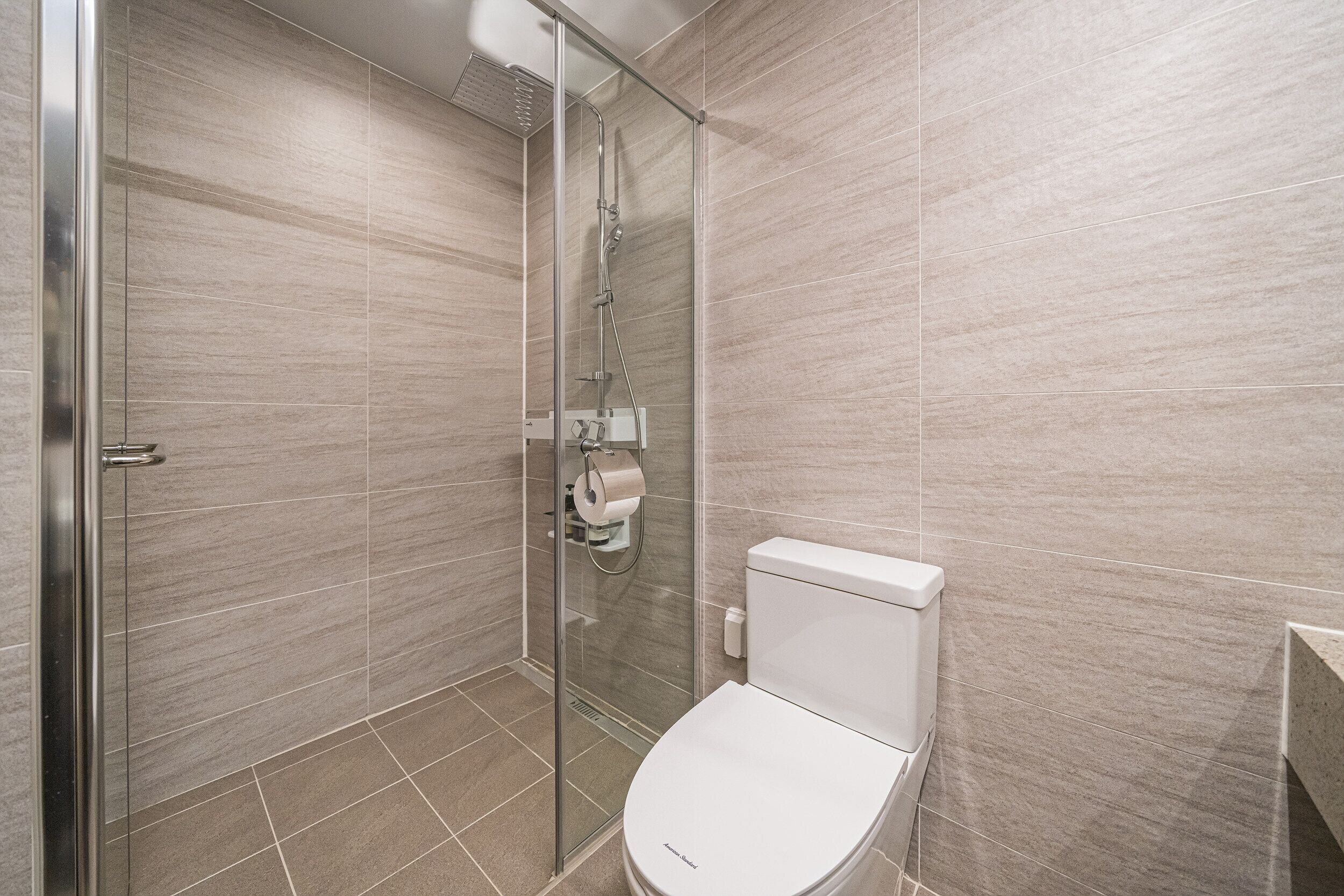 A modern bathroom with a glass shower enclosure, a toilet, and a tiled floor.