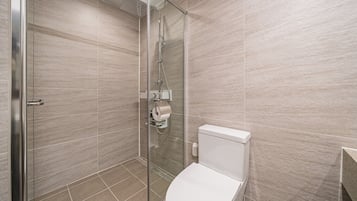 A modern bathroom with a glass shower enclosure, a toilet, and a tiled floor.
