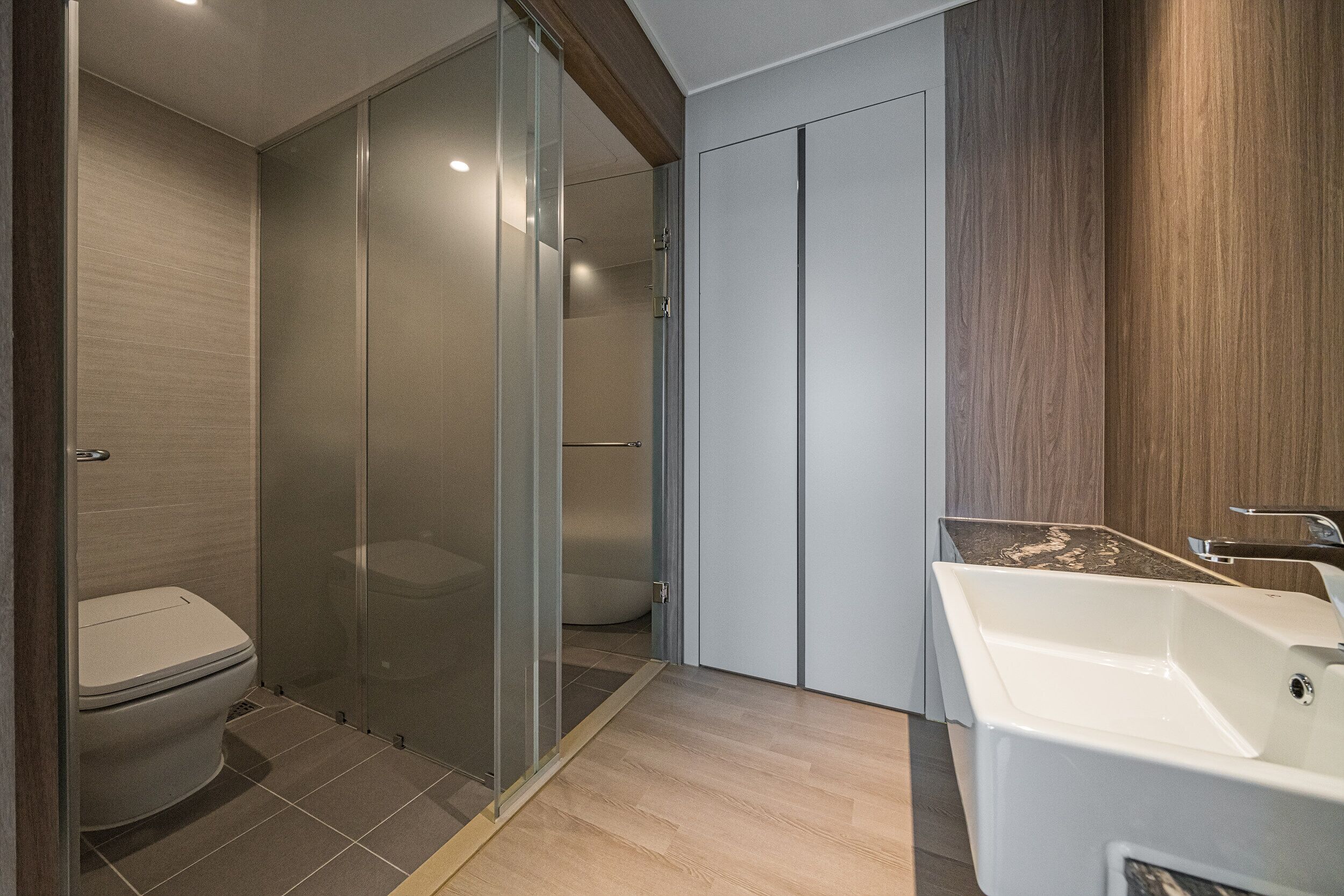 Un baño moderno con cabina de ducha de vidrio, inodoro blanco y lavamanos blanco con encimera de madera.