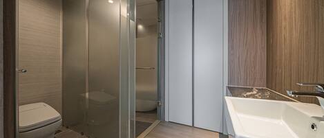 Un baño moderno con cabina de ducha de vidrio, inodoro blanco y lavamanos blanco con encimera de madera.