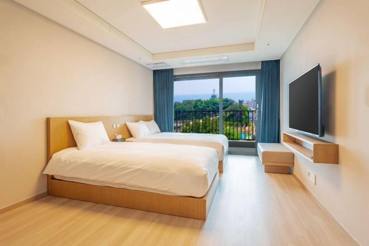 Habitación de hotel con dos camas, televisión y balcón con vista a la ciudad.
