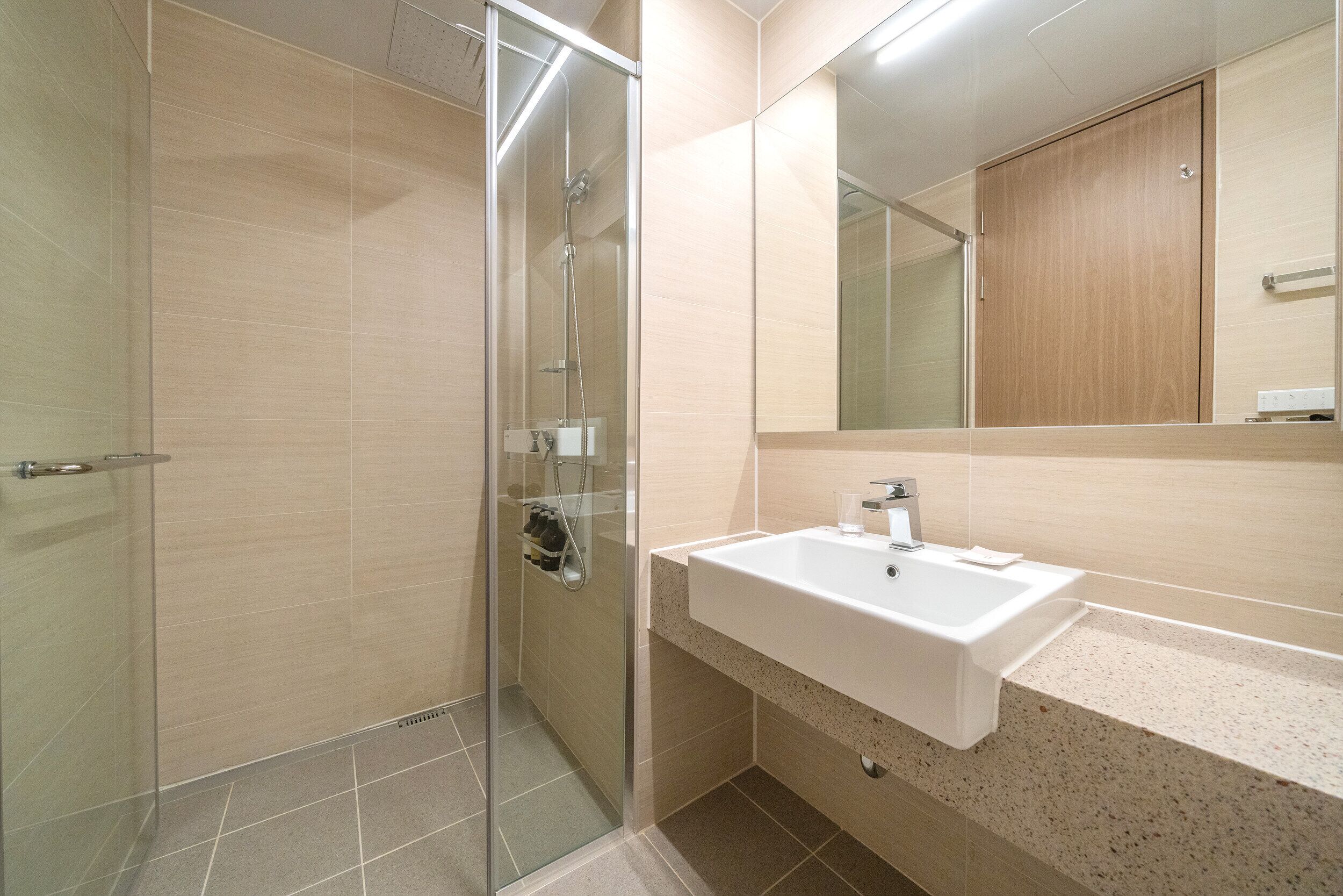 Un baño moderno con cabina de ducha de vidrio, lavamanos blanco y mueble de madera.