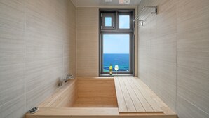 Un baño moderno con una bañera de madera, un ventanal con vistas al mar y un perchero para toallas.