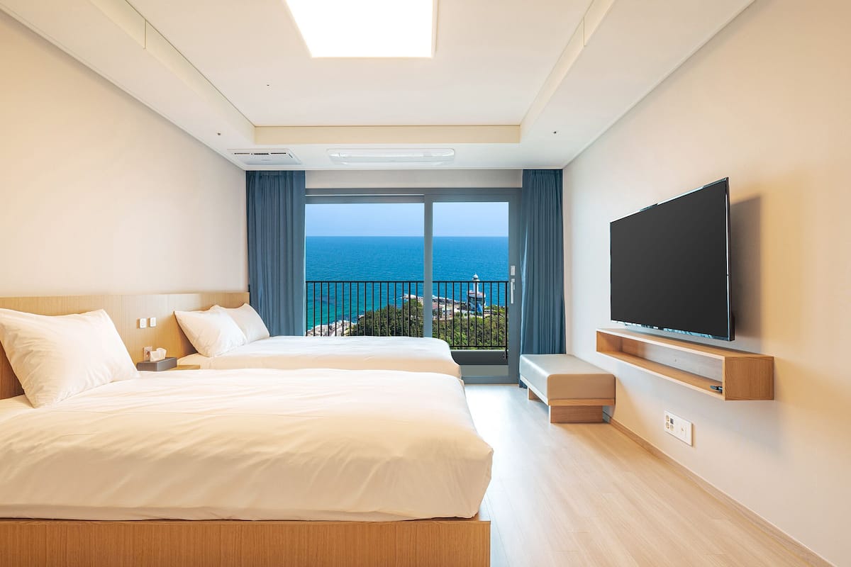 Una habitación de hotel con dos camas, televisión y balcón con vista al mar.