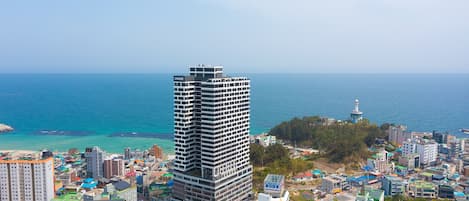 A high-rise building with multiple floors, surrounded by a coastal cityscape with visible roads and smaller buildings.