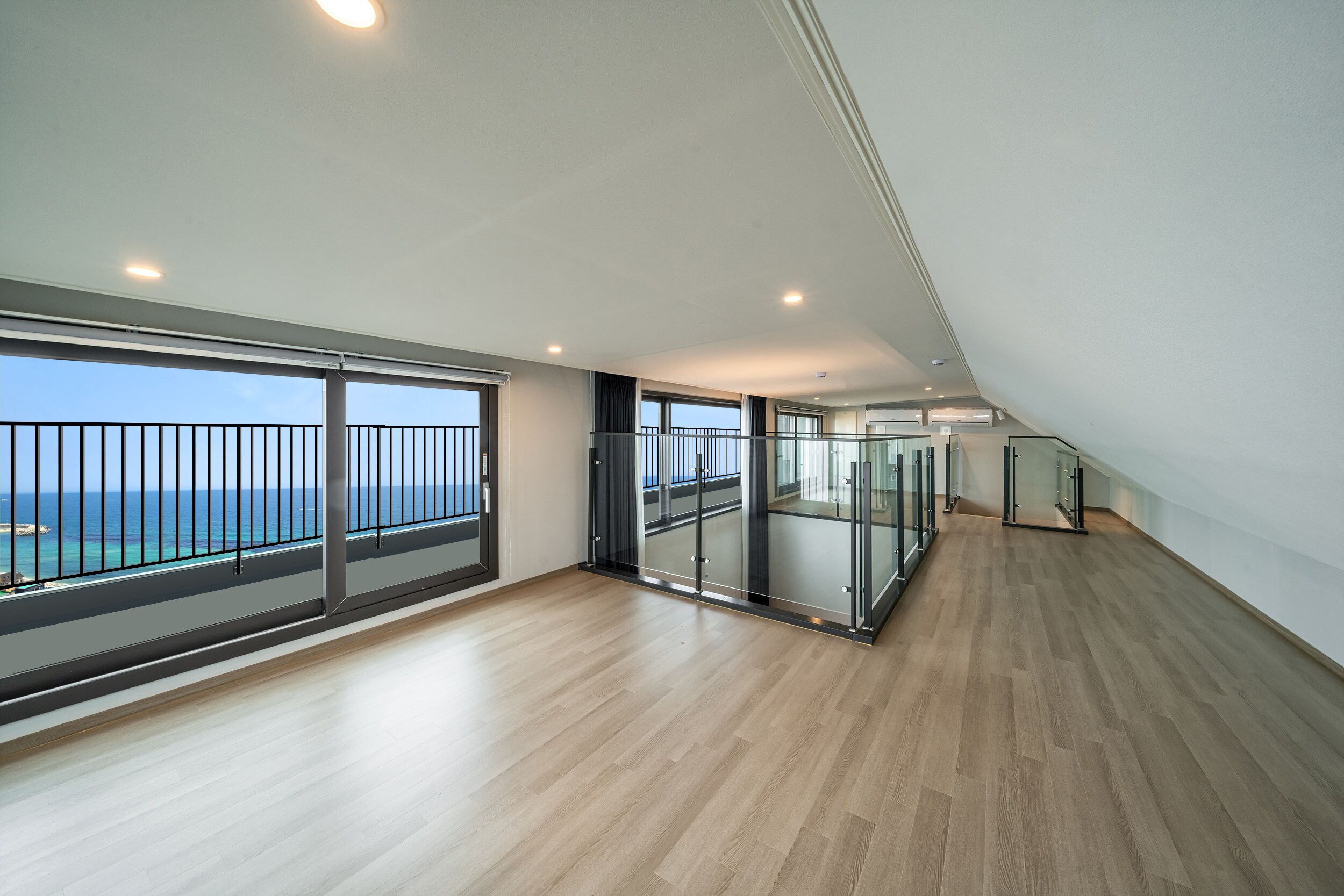En rummelig balkon med havudsigt, et moderne interiør med trægulve og gelænder af glas.