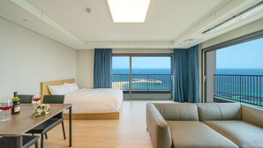 Habitación de hotel con cama, sofá, mesa de comedor y vistas al mar.