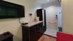A small room with a flat-screen TV mounted on the wall, a desk with a computer, a microwave, and a cabinet. - Darul Salam Orkid Inn (Kerteh)