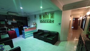 A reception area with a desk, a black leather sofa, and framed pictures on the wall. - Darul Salam Orkid Inn (Kerteh)
