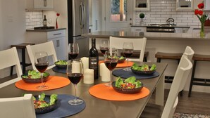 Een moderne keuken met witte kastjes, een roestvrijstalen koelkast, en een eethoek met oranje en blauwe placemats.
