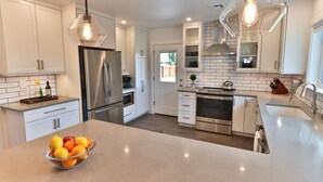 Een moderne keuken met witte kasten, roestvrijstalen apparatuur en een centraal eiland met een fruitschaal.
