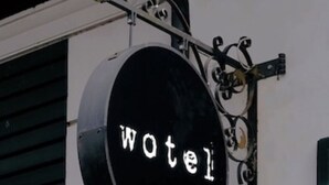 Un letrero negro con la palabra "Wotel" en letras blancas, sujeto a una estructura metálica con una luz esférica encima.
