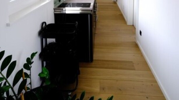 Un estrecho pasillo con una zona de cocina en un lado, vigas de madera en el techo y una escalera que conduce a un nivel superior.