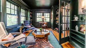 Um quarto acolhedor com uma janela grande, uma mesa de centro de vidro, um tapete com padrão de zebra e uma estante de livros.