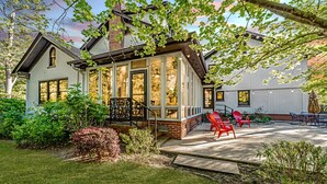 Uma casa com varanda coberta, chaminé de tijolos e um jardim bem cuidado.