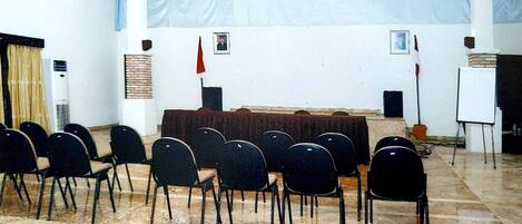 A room with a tiled floor, a white wall with a window, and a black chair arrangement.