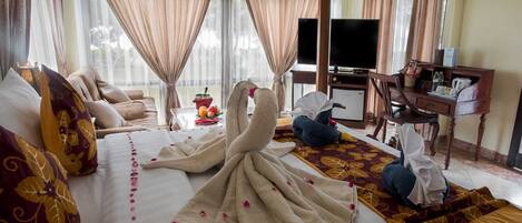 A hotel room with a large bed, a desk, a television, and a view of the outdoors.