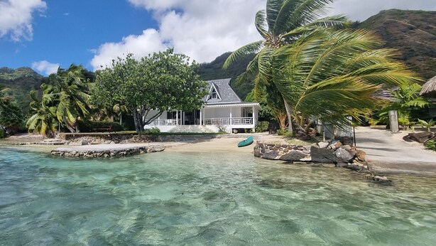 Ein Anwesen am Strand mit einem Haus, Palmen und klarem Wasser.