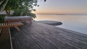 Eine Holzterrasse mit einer Bank und einem Bett, mit Blick auf ruhiges Gewässer.
