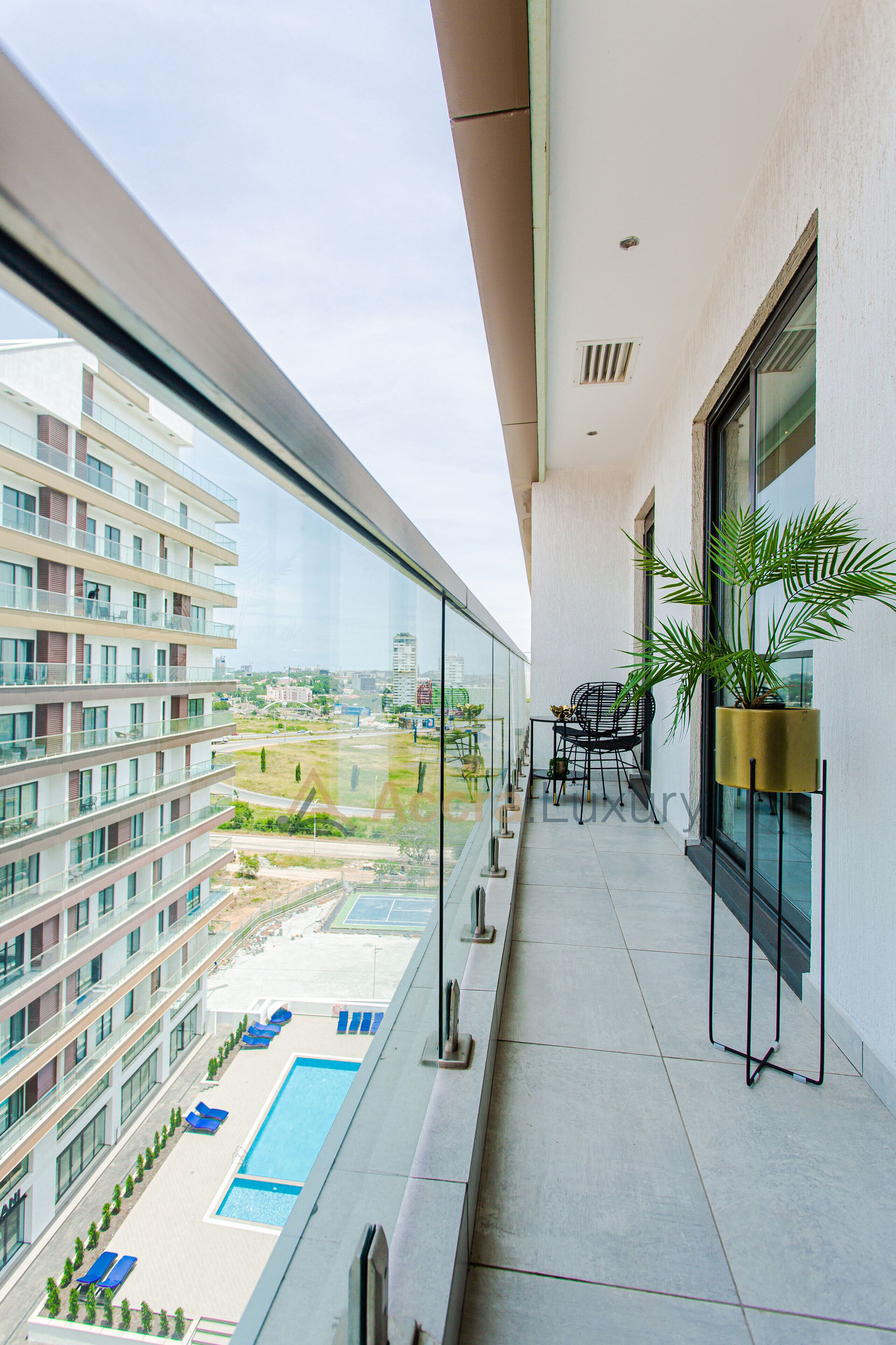 A balcony with a glass railing, a pool, lounge chairs, and a table with chairs.