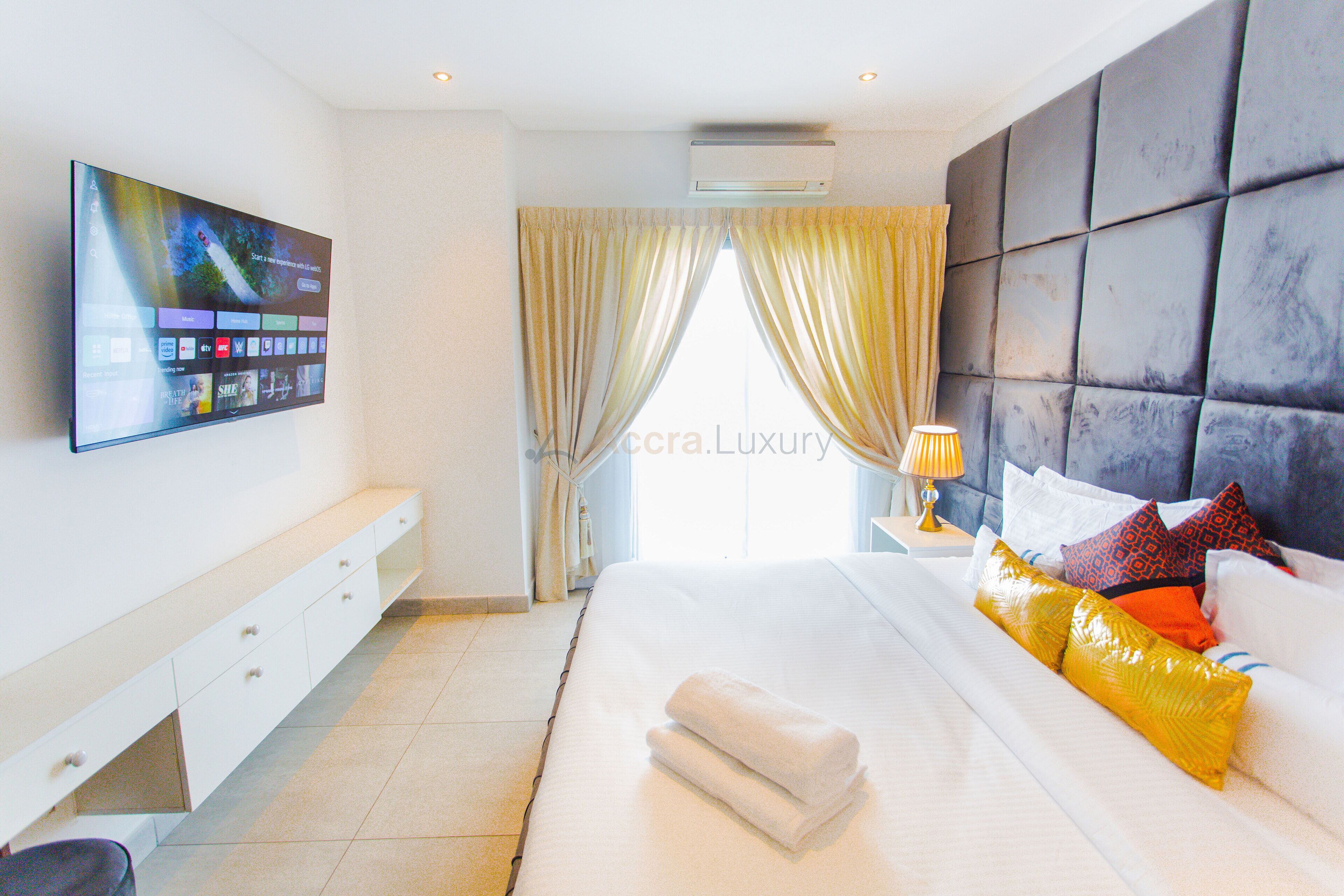 Una habitación de hotel moderna con una cama grande, un televisor de pantalla plana montado en la pared, una mesita de noche y una ventana con cortinas.