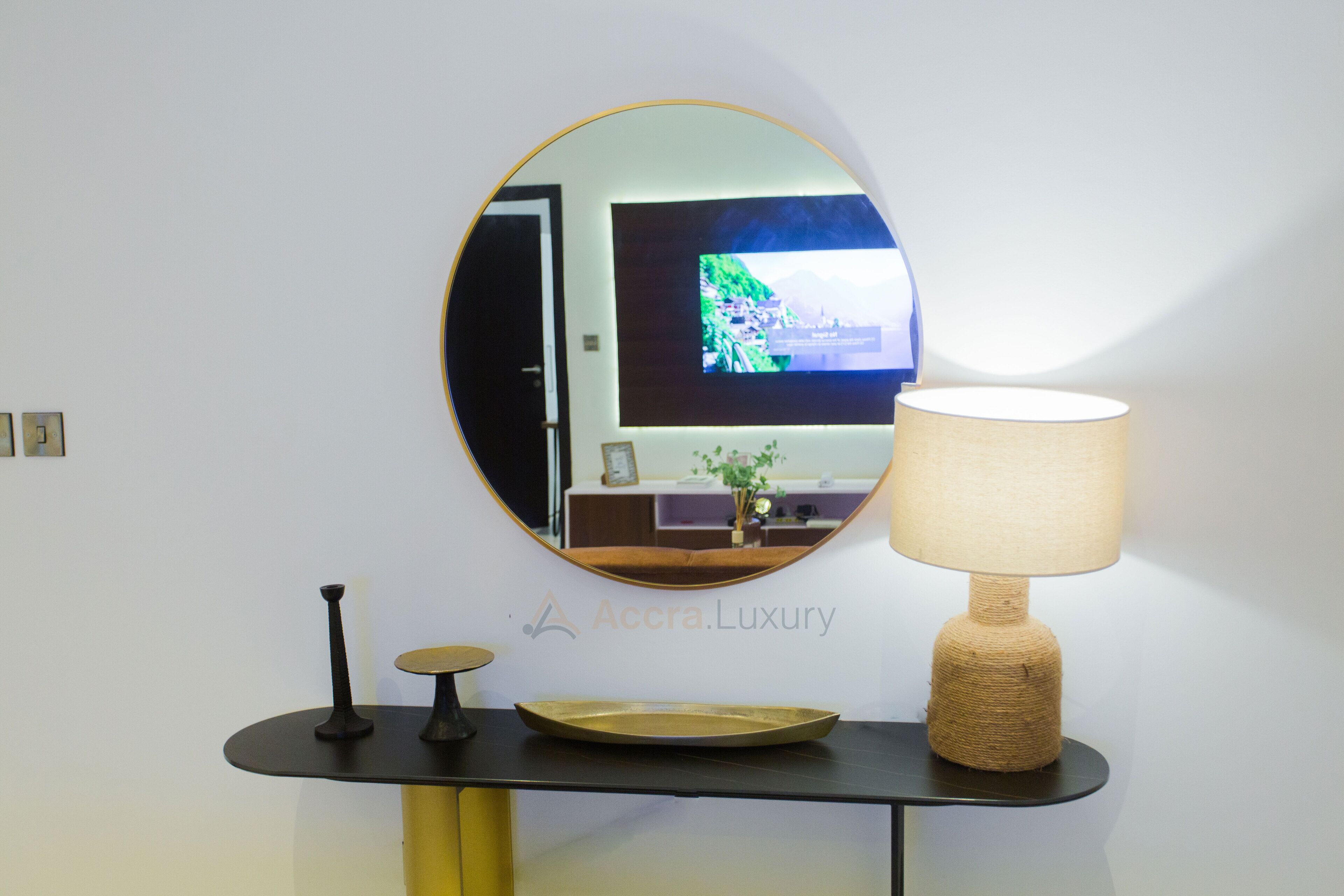 Un interno moderno con uno specchio rotondo che riflette una stanza, un tavolo con una lampada e un televisore a parete.