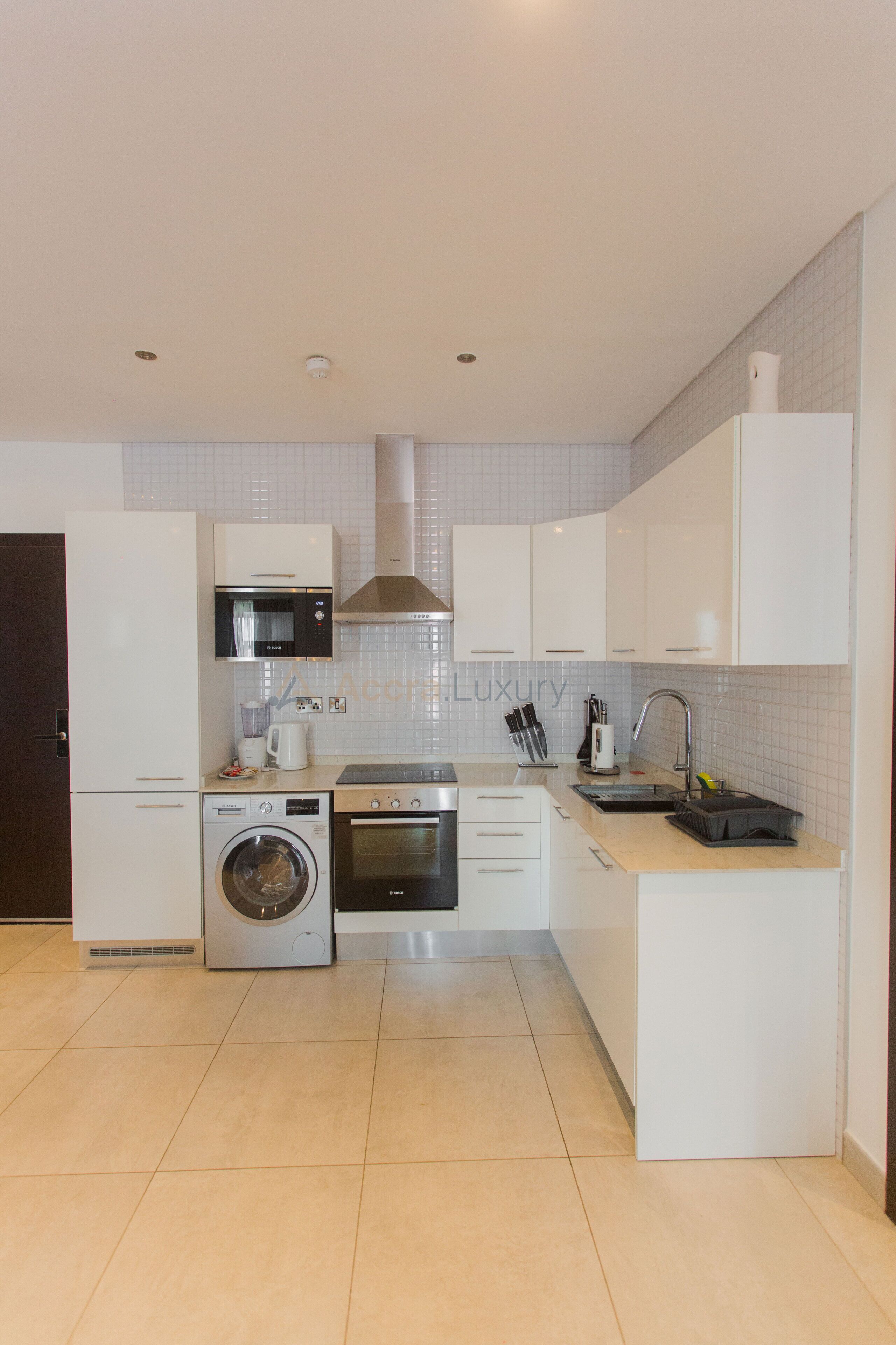A modern kitchen with white cabinetry, a built-in microwave, oven, and washing machine.