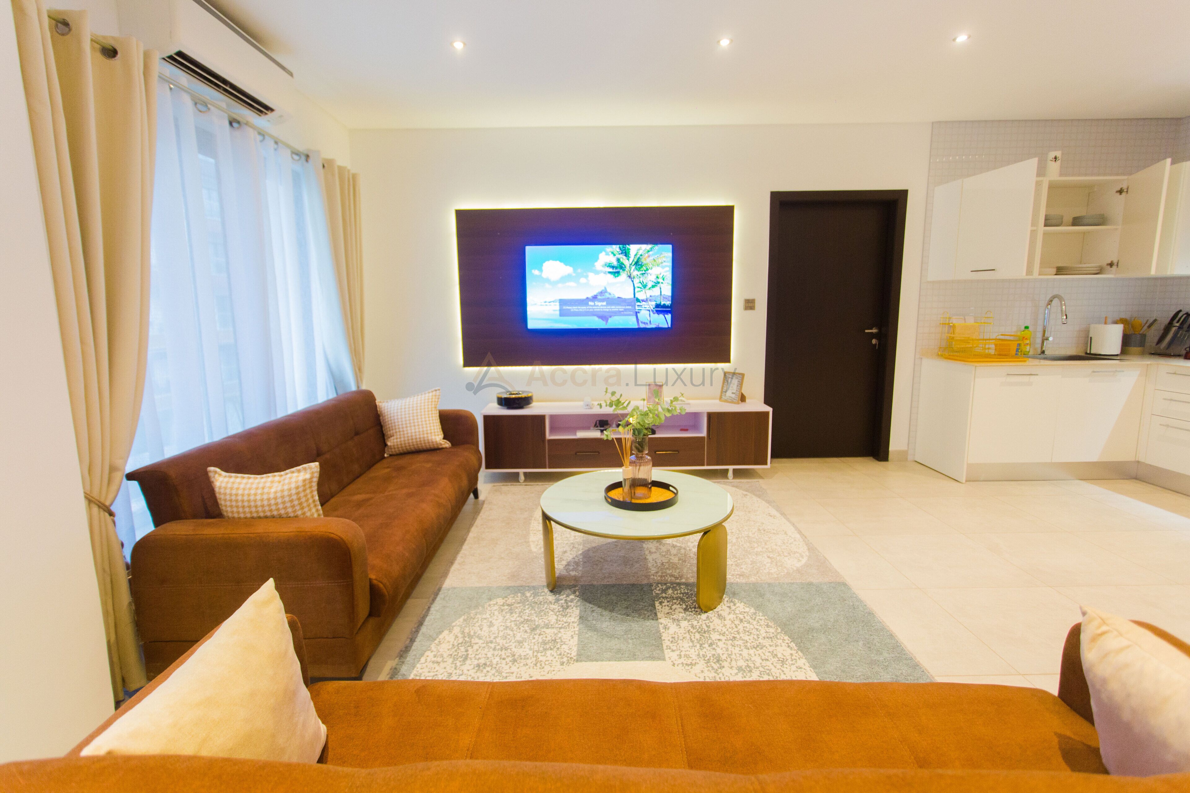 A modern living room with a brown sofa, a coffee table, and a flat-screen TV mounted on the wall.
