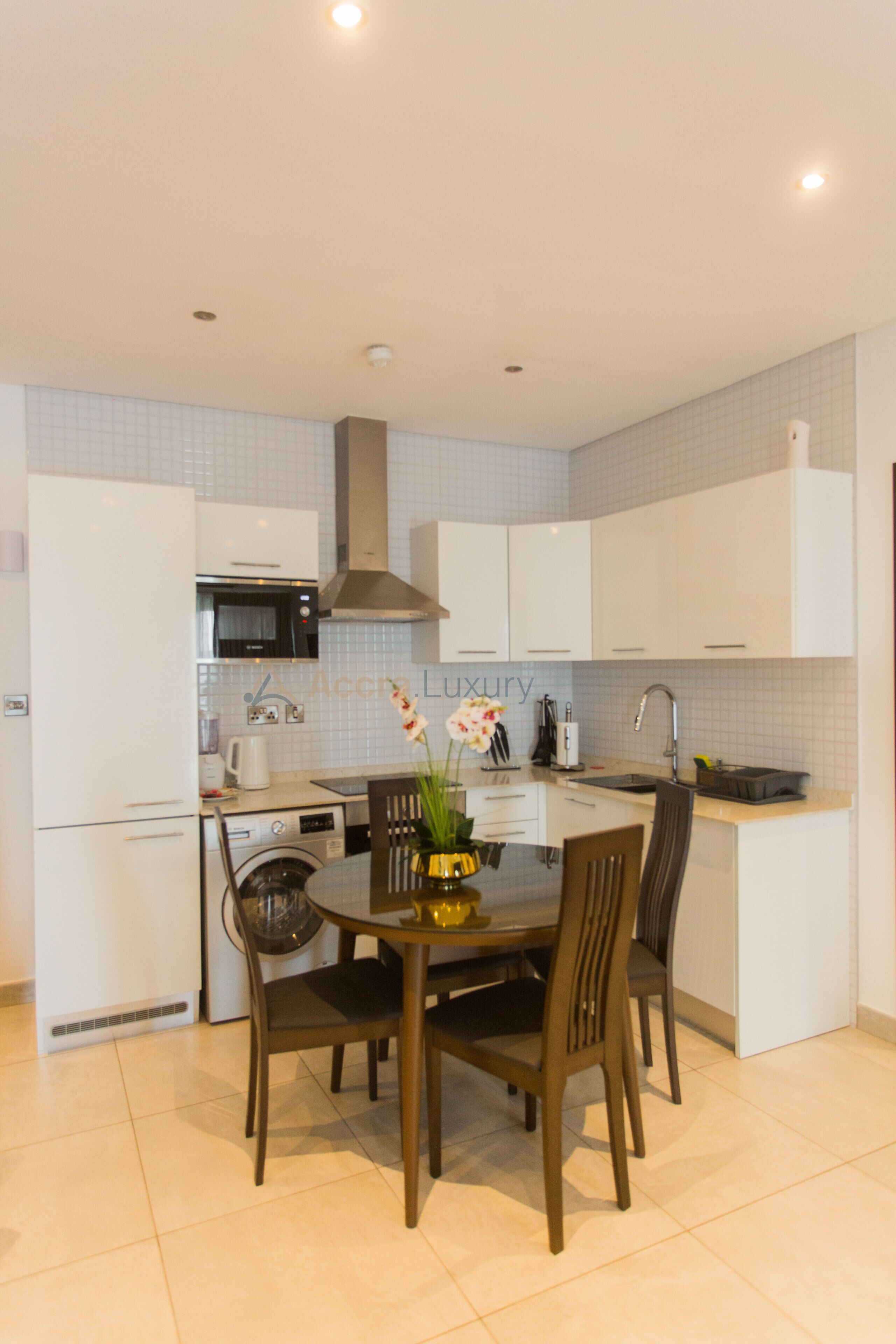 A modern kitchen with white cabinets, a built-in oven, and a dining area with a table and chairs.