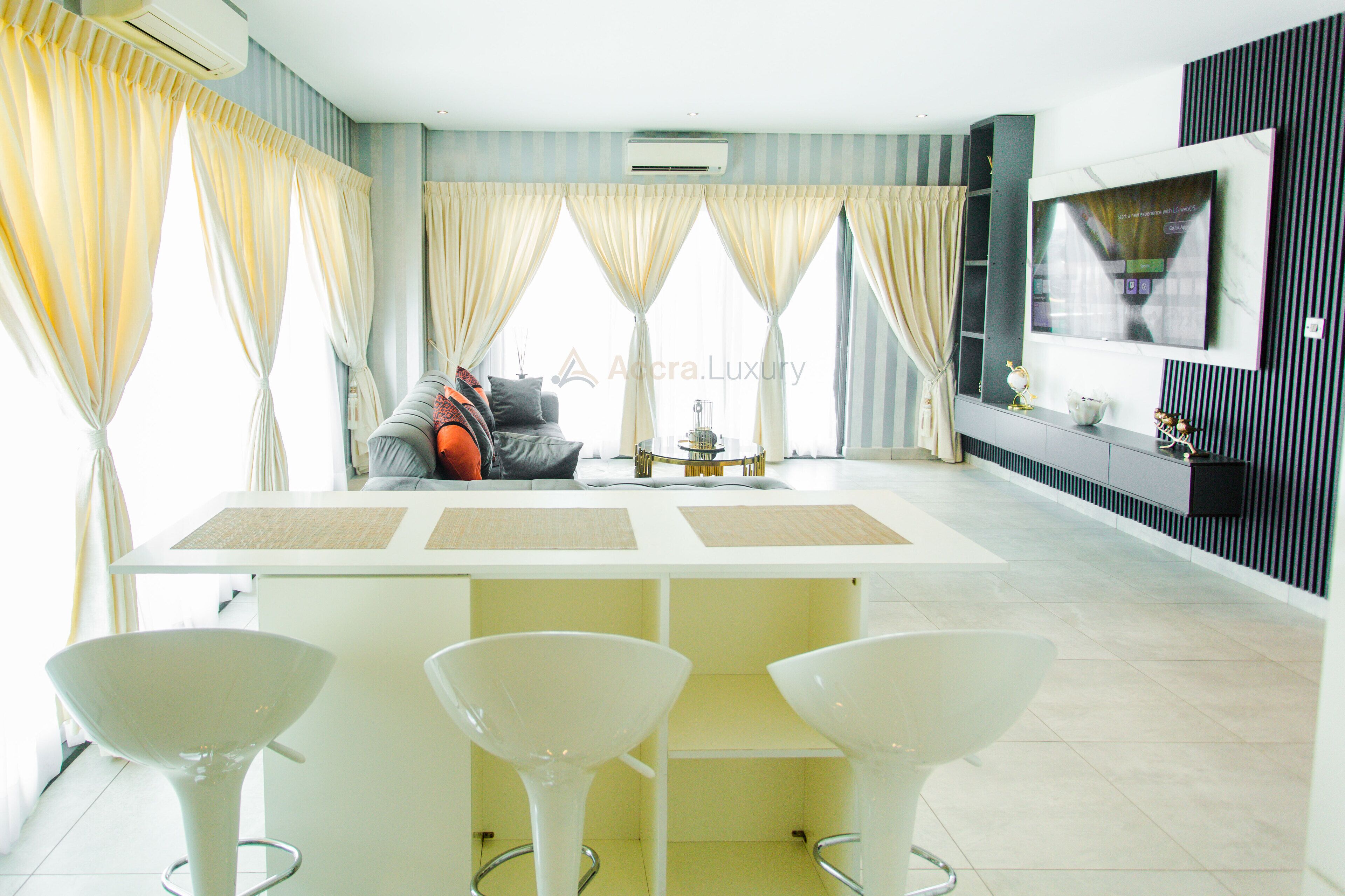 A modern living room with a sofa, a TV, and a dining area with white chairs.