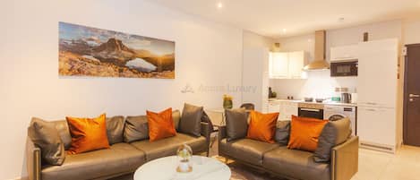 Una sala de estar moderna con dos sofás de cuero, una mesa de centro de mármol y un cuadro de paisaje grande en la pared.