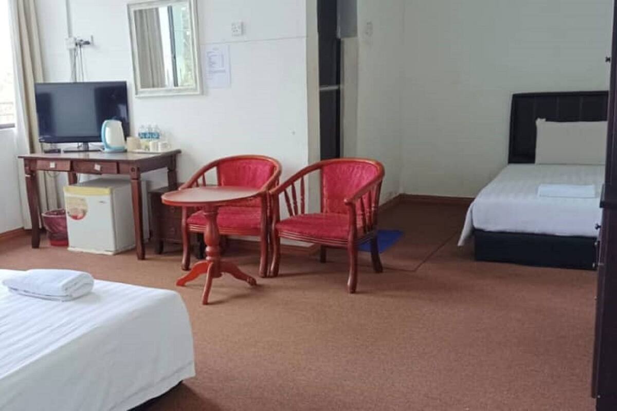 Ein Hotelzimmer mit zwei Betten, einem Schreibtisch mit Fernseher, einem kleinen Kühlschrank und zwei roten Stühlen.