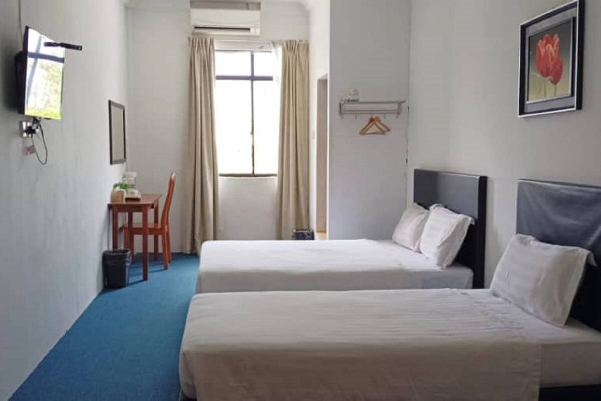 Ein Hotelzimmer mit zwei Betten, einem Schreibtisch, einem Stuhl, einem Fernseher und einem Fenster mit Vorhängen.