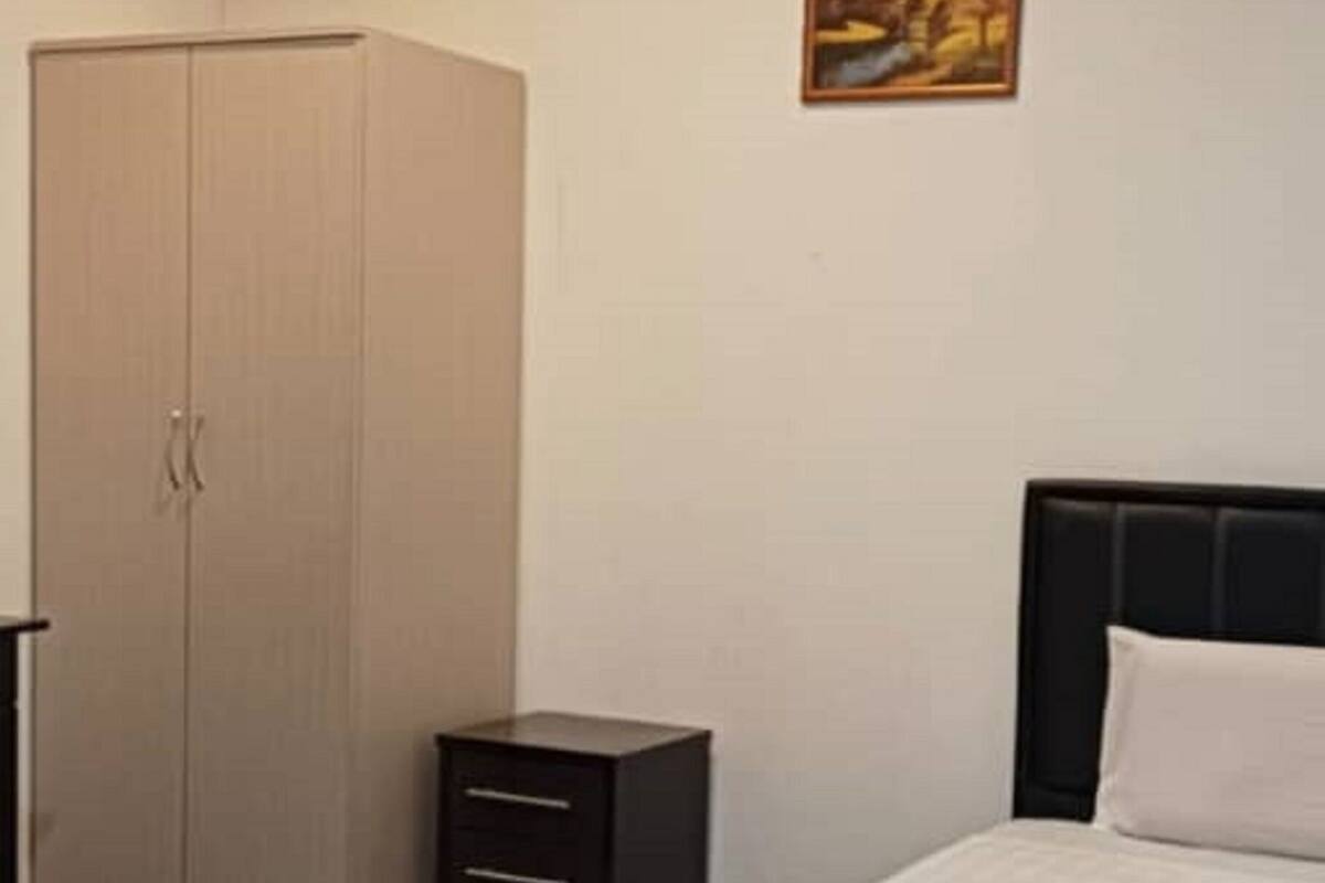 Ein Hotelzimmer mit Bett, Schrank, Nachttisch und einem Gemälde an der Wand.