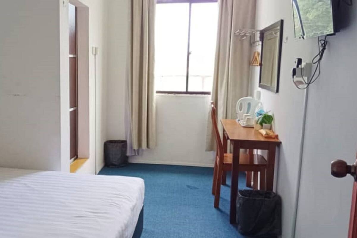 Ein Hotelzimmer mit einem Bett, einem Schreibtisch und einem Stuhl. Es gibt ein Fenster mit Vorh ängen, eine Tür und einen an der Wand befestigten Fernseher.