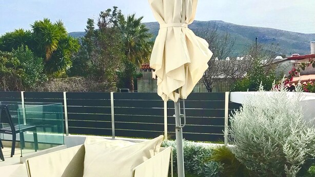 Un patio al aire libre con un sofá blanco, una mesa redonda y un gran paraguas.