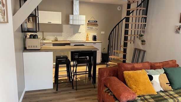 Une cuisine moderne dotée d’un îlot central, de tabourets de bar noirs et d’un escalier avec une rampe en bois.
