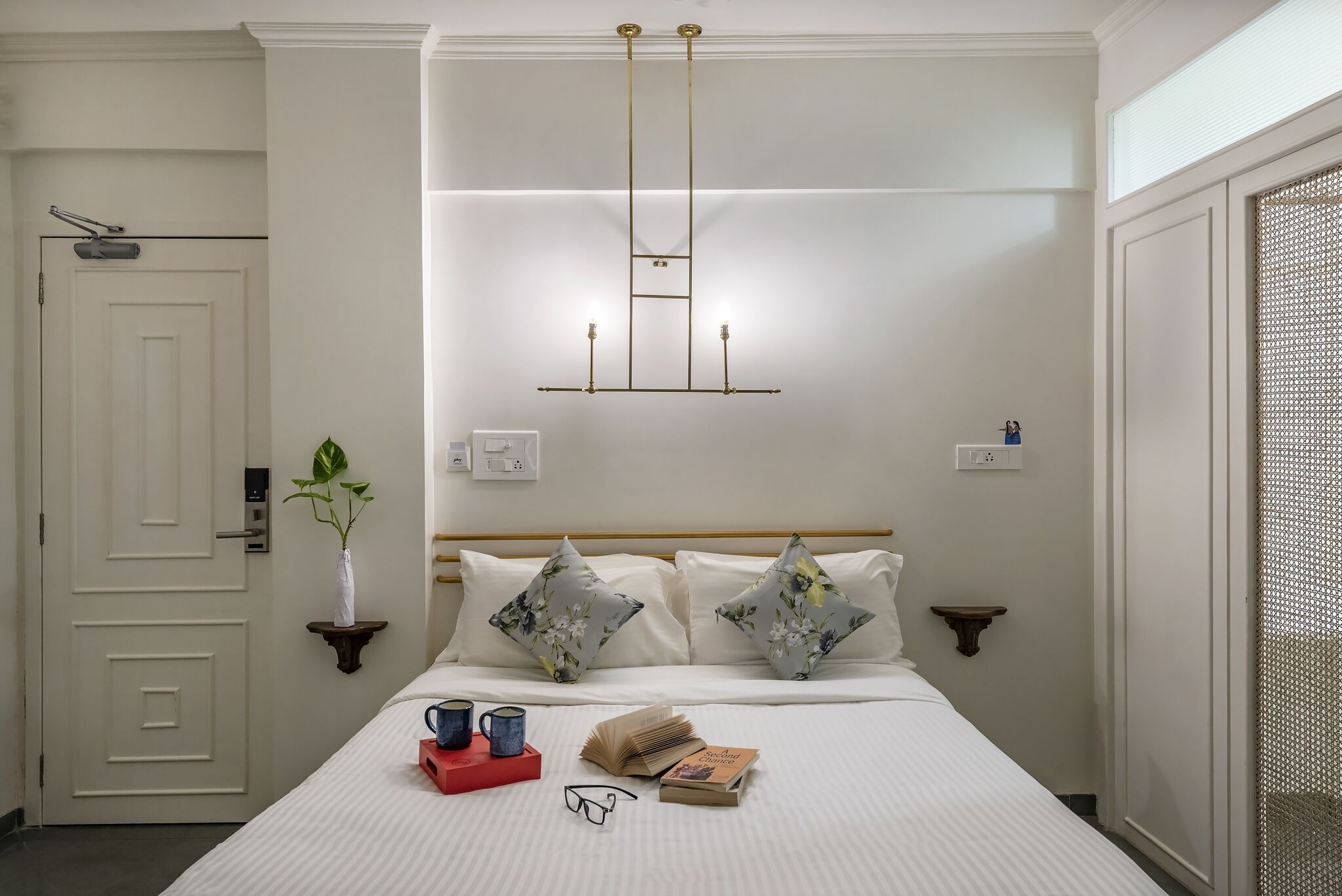 A neatly arranged hotel room with a bed, bedside tables, a wall-mounted light fixture, and a door.