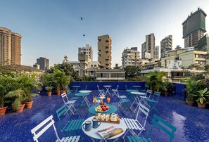 A rooftop pool area with blue-tiled flooring, outdoor seating, and a table set with food and drinks. - Hotel Kemps Corner (Mumbai)