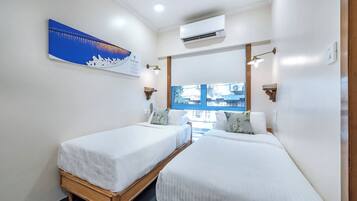Een hotelkamer met twee enkele bedden, een groot raam, een airconditioning en een kunstwerk aan de muur.