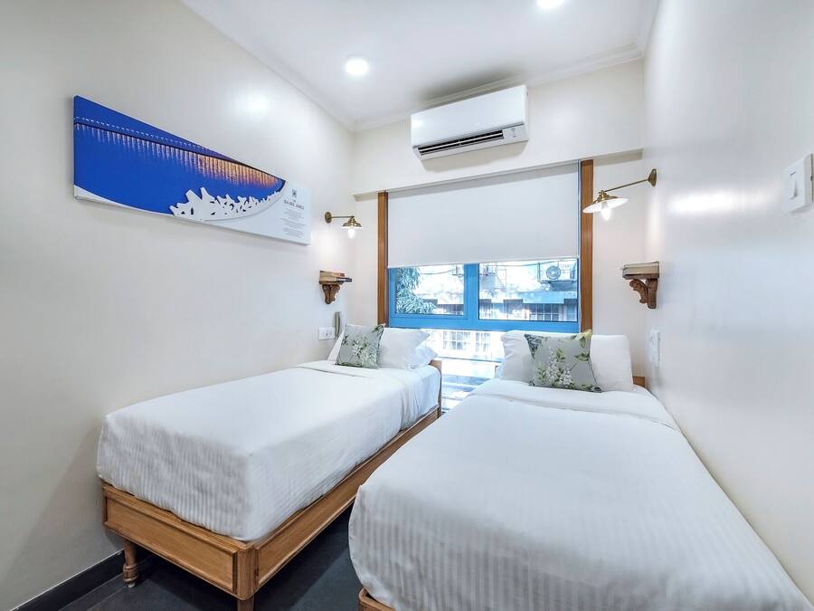 Een hotelkamer met twee enkele bedden, een groot raam, een airconditioning en een kunstwerk aan de muur.