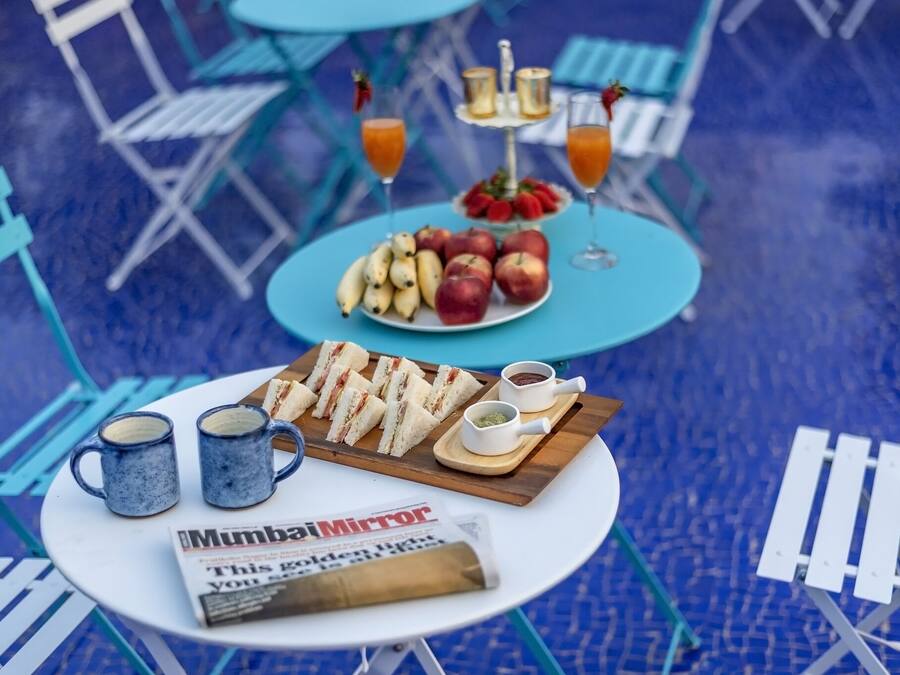 Una mesa con un periódico, dos tazas, una bandeja de sándwiches y un plato de fruta.