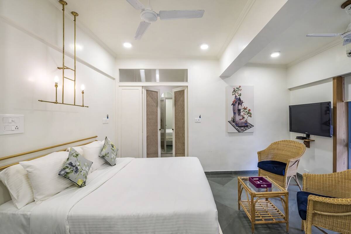 A hotel room with a bed, a television, a wicker chair, and a ceiling fan.