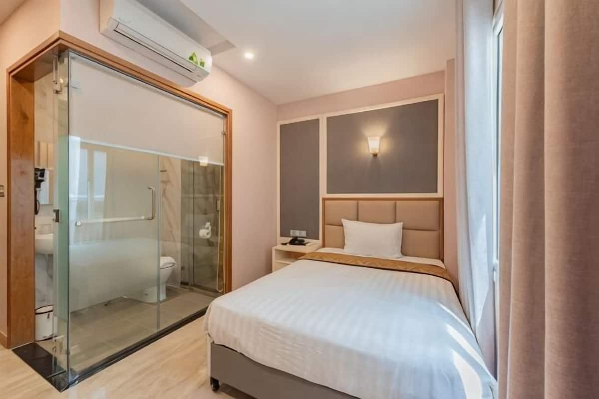 Une chambre d’hôtel dotée d’une douche en verre, d’un lit avec une tête de lit, d’une table de chevet et d’une petite table de nuit.